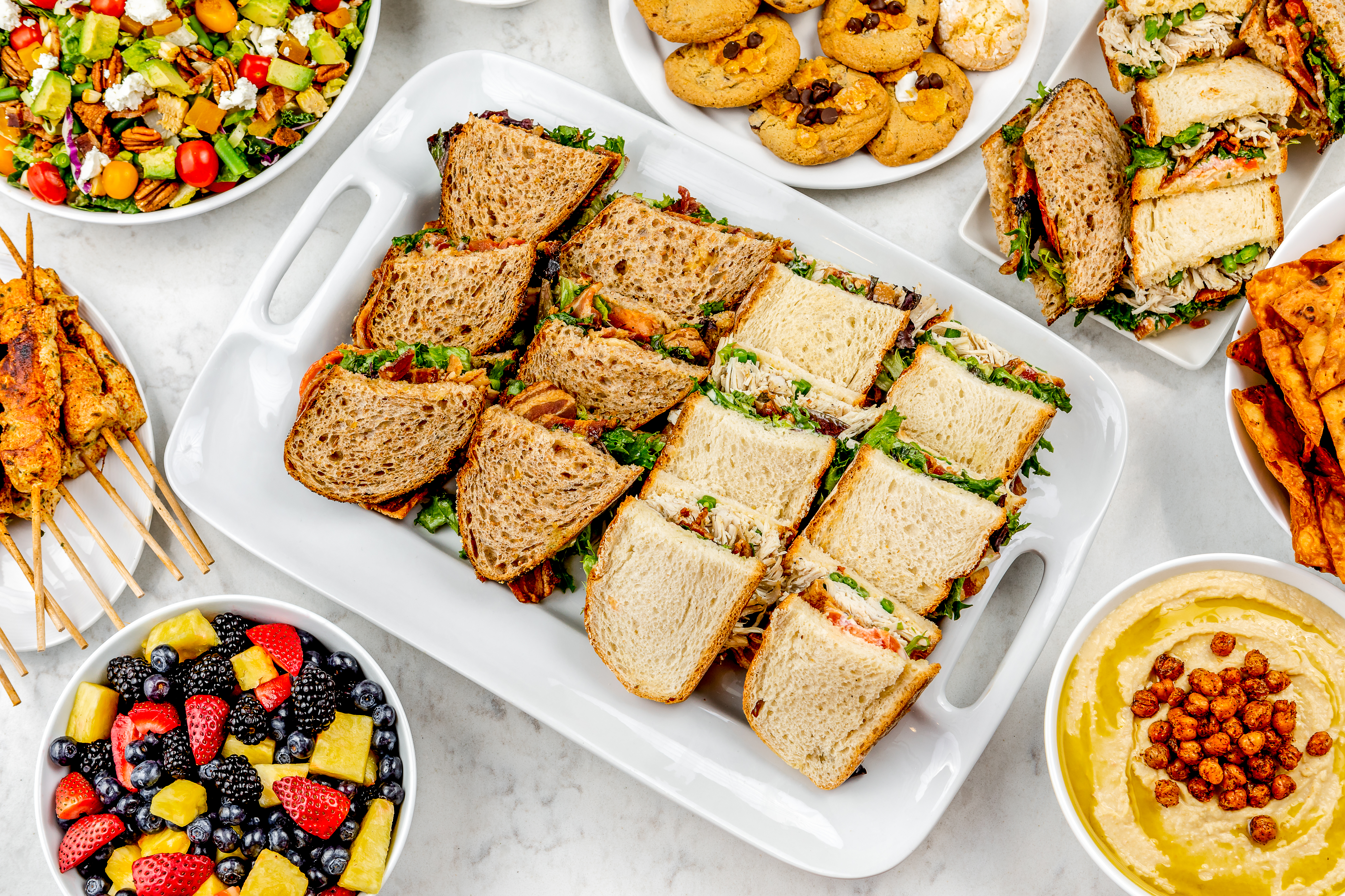 Catering platers with sandwiches, salads, and cookies
